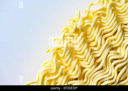 Eine Makroaufnahme eines Blocks trockener, gelber, welliger Instant-Nudeln, die ihre komplexe Textur und Muster vor einem sauberen weißen Hintergrund zur Schau stellen Stockfoto