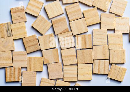 Hohe Ansicht von zahlreichen leeren, natürlichen Holzquadern, die zufällig über eine saubere weiße Oberfläche verstreut sind. Perfekt für Brettspielkonzepte, Bildung Stockfoto