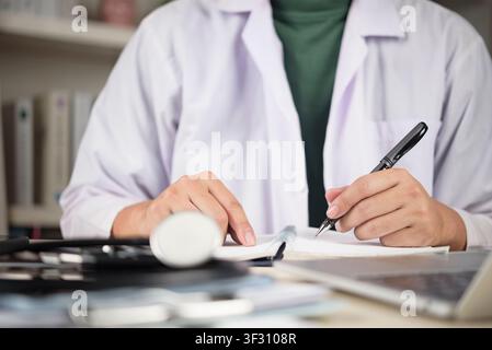 Männlicher Arzt oder Medizinstudent schreibt Notizen in ein Notizbuch mit Stethoskop und Laptop auf dem Schreibtisch. Konzept der medizinischen Ausbildung, klinischen Forschung, an Stockfoto
