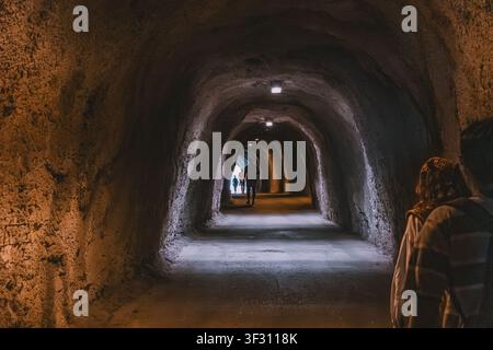 23. Mai 2026, Becici, Montenegro: Dunkler unterirdischer Tunnel mit Menschen, die auf fernes Licht zugehen und eine Atmosphäre von Mystik und Reise erzeugen Stockfoto