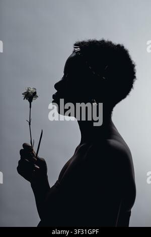 Schwarze erwachsene Frau, die eine Blume im Profil für Beauty-Branding hält Stockfoto