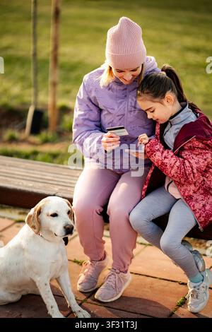 Mutter und Tochter verwenden Kreditkarte für Online-Einkäufe im Park Stockfoto