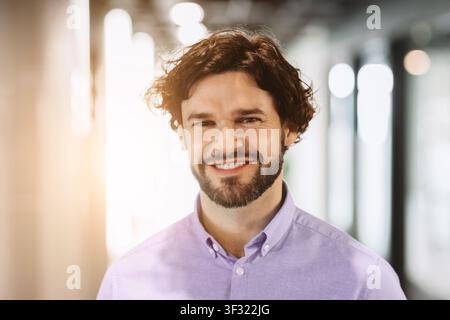 Lächelnder Mann steht in einer hellen Büroumgebung während der Tagesstunden Stockfoto