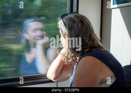 Reife Frau sitzt im Zug und schaut auf die Reflexion im Fenster Stockfoto