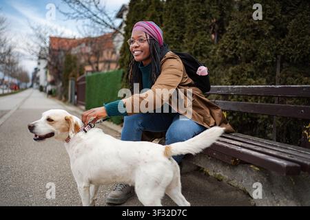 Glückliche schwarze Frau, die auf der Parkbank sitzt und Hund streichelt Stockfoto