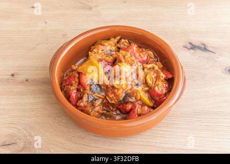 Rustikale sizilianische Caponata mit geschmorten Auberginen, Paprika und Tomaten in einer Terracottaschüssel auf einem Holztisch. Stockfoto
