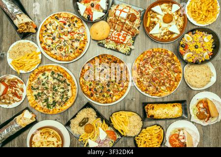 Massives Overhead-Festmahl mit vier Pizzen, Gyros, Pommes, Reis, Feta-Salaten und Burritos Stockfoto