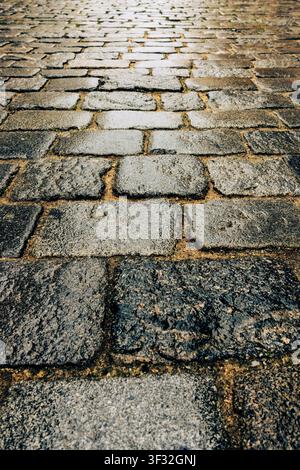 Niedriger Nahaufnahme einer alten unebenen Kopfsteinpflasterstraße, die verwitterte Steinblöcke, Textur und Perspektive zeigt Stockfoto
