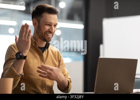 Froher kaukasischer Mann, der während eines Videoanrufs aus der Ferne arbeitet, Büroumgebung, Geschäftskonzept Stockfoto