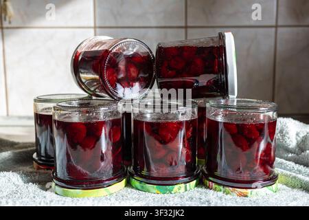 Sechs Gläser dunkelroter Kirschmarmelade in zwei Reihen angeordnet, hausgemachte süße Beerenkonfitüre und Einmachvorbereitung auf rustikalem Küchentisch, Frontansicht Stockfoto