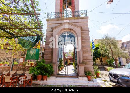 Lesbos, Griechenland – 23. April 2026: Verzierter Steineingang des Glockenturms mit einem offenen Eisentor führt in den Innenhof der Saint-Basil-Kirche im Dorf Stockfoto