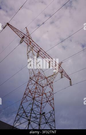 Hochspannungsmast-Struktur, die Stromleitungen gegen einen bewölkten Himmel stützt Stockfoto
