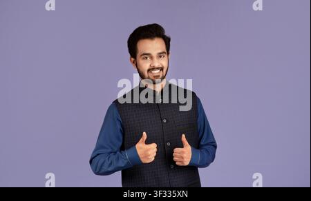 Ein fröhlicher Mann indischer Herkunft, der mit Zustimmung den Daumen nach oben zeigt Über fliedem Hintergrund Stockfoto