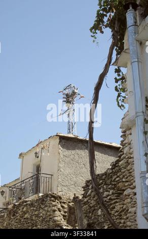 Kontrast in Bubion mit dem Stamm einer Weinranke, die die rustikale Mauer zur Terrasse hin hinaufklettert, und einer hochmodernen Antenne auf einem kleinen alten Haus Stockfoto