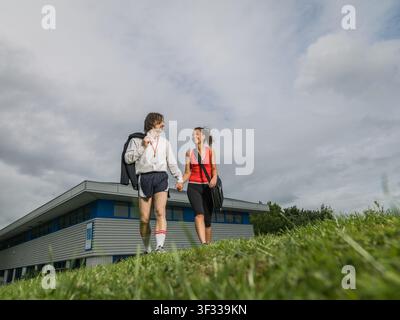 Paar geht vom Büro weg, hält sich an den Händen und trägt Sportkleidung Stockfoto