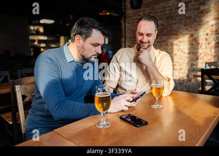 Zwei Männerfreunde trinken Bier und unterhalten sich mit dem Smartphone in der Kneipe Stockfoto