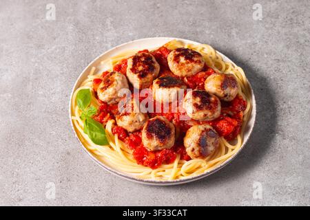 Ein Teller mit klassischen Spaghetti, garniert mit gebräunten Fleischbällchen und reichhaltiger Tomatensauce auf einem leichten Keramikgericht. Stockfoto