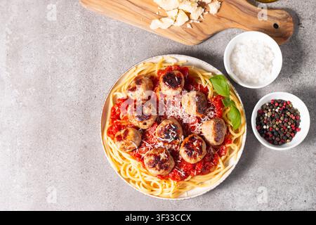 Ein Teller mit klassischen Spaghetti, garniert mit gebräunten Fleischbällchen und reichhaltiger Tomatensauce auf einem leichten Keramikgericht. Stockfoto