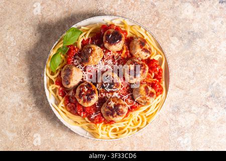 Ein Teller mit klassischen Spaghetti, garniert mit gebräunten Fleischbällchen und reichhaltiger Tomatensauce auf einem leichten Keramikgericht. Stockfoto