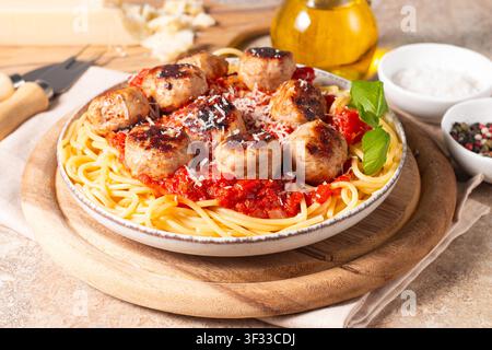 Ein Teller mit klassischen Spaghetti, garniert mit gebräunten Fleischbällchen und reichhaltiger Tomatensauce auf einem leichten Keramikgericht. Stockfoto