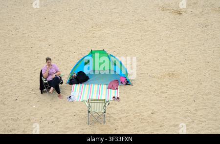 eine Frau, die vor ihrem Windbreaker-Zelt an einem sandigen Strand am Meer in Clacton-on-Sea, UK, sitzt Stockfoto