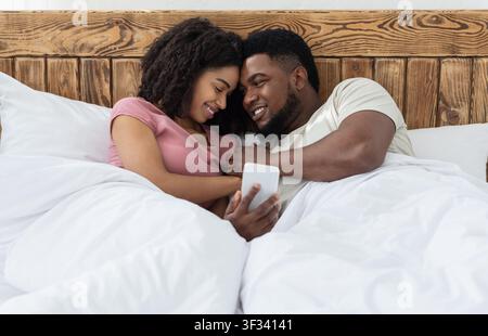 Emotionales Paar kuscheln und Fotos zusammen auf dem Smartphone anschauen Stockfoto