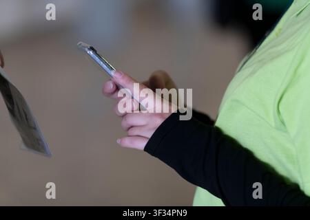 Teilnehmer, der ein grünes Hemd trägt und ein Smartphone neben einem Ausweisetag an einem Geschäftsevent hält. Stockfoto