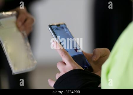 Nahaufnahme eines Teilnehmers, der ein Smartphone neben einem Event-Abzeichen während der Konferenzanmeldung verwendet. Stockfoto