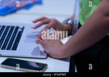 Nahaufnahme von Händen, die auf einem Laptop neben einem Smartphone an einem Anmeldeschalter für Veranstaltungen tippen. Stockfoto
