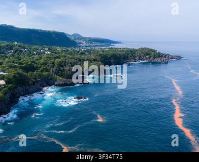 Luftaufnahme des Kadowakisaki-Leuchtturms, der auf den schroffen Klippen der Izu-Halbinsel gelegen ist, umgeben von üppigen grünen Wäldern und dem tiefblauen Meer in I Stockfoto