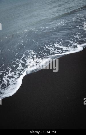 Schwarze Sandstrandwellen Stockfoto