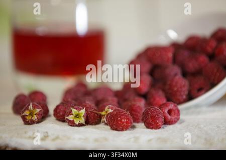 Eine Nahaufnahme mit selektivem Fokus auf ein paar frischen roten Himbeeren, die auf einer weißen Spitzendecke verstreut sind. Im weichgezeichneten Hintergrund Stockfoto