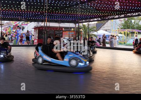 Menschen haben Spaß beim Fahren mit Stoßstangen in einem Vergnügungspark mit bunten Lichtern unter einem Baldachin in der Nacht. Bulgarien, Varna, 20. Juli 2026 Stockfoto