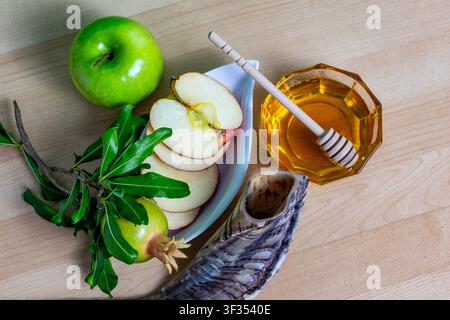 Jüdische Neujahrssymbole, darunter Äpfel, Honig, Granatapfel und ein Schofar auf einem Holztisch Stockfoto