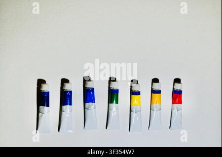 Reihe von Farbe Vertikale Hochwinkelaufnahme von bunten Acryl- oder Ölfarbtuben, die ordentlich in einer Reihe auf einem weißen Hintergrund angeordnet sind, mit Platz für Text. Minimalistischer Hintergrund ideal für Kunststudio, Malerei, Kunstbedarfskatalog, Design und pädagogische Konzepte. auf weißer Oberfläche mit Kopierraum. Hochwertiges Foto Stockfoto