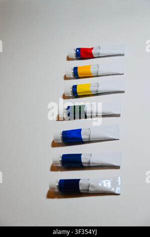 Reihe von Farbe Vertikale Hochwinkelaufnahme von bunten Acryl- oder Ölfarbtuben, die ordentlich in einer Reihe auf einem weißen Hintergrund angeordnet sind, mit Platz für Text. Minimalistischer Hintergrund ideal für Kunststudio, Malerei, Kunstbedarfskatalog, Design und pädagogische Konzepte. auf weißer Oberfläche mit Kopierraum. Hochwertiges Foto Stockfoto