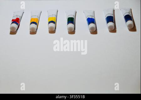 Reihe von Farbe Vertikale Hochwinkelaufnahme von bunten Acryl- oder Ölfarbtuben, die ordentlich in einer Reihe auf einem weißen Hintergrund angeordnet sind, mit Platz für Text. Minimalistischer Hintergrund ideal für Kunststudio, Malerei, Kunstbedarfskatalog, Design und pädagogische Konzepte. auf weißer Oberfläche mit Kopierraum. Hochwertiges Foto Stockfoto