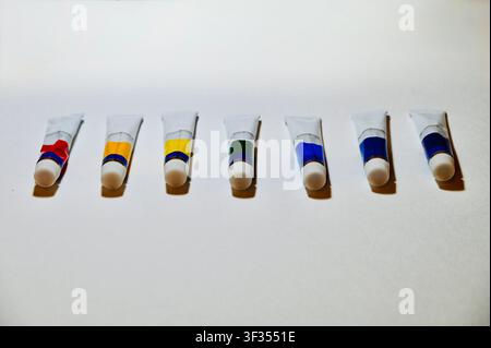 Reihe von Farbe Vertikale Hochwinkelaufnahme von bunten Acryl- oder Ölfarbtuben, die ordentlich in einer Reihe auf einem weißen Hintergrund angeordnet sind, mit Platz für Text. Minimalistischer Hintergrund ideal für Kunststudio, Malerei, Kunstbedarfskatalog, Design und pädagogische Konzepte. auf weißer Oberfläche mit Kopierraum. Hochwertiges Foto Stockfoto