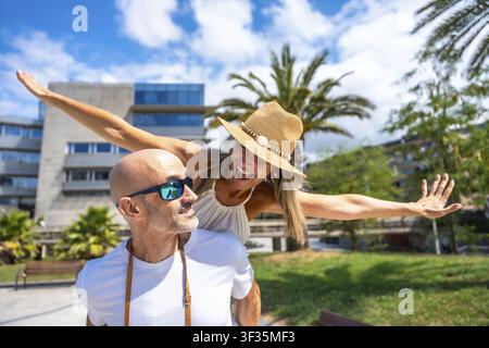 Reifes Paar hat Spaß mit einer Huckepackfahrt im Freien, feiert Liebe und Freiheit im Sommerurlaub unter einem blauen Himmel Stockfoto