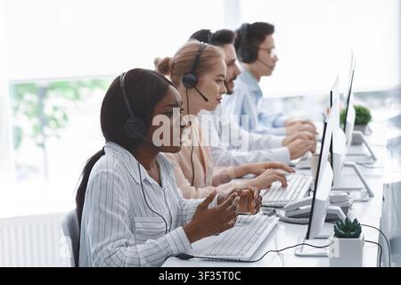 Gestresste Callcenter-Managerin mit Headset, die sich mit den Beschwerden der Kunden und ihrem Team im Büro anhört Stockfoto