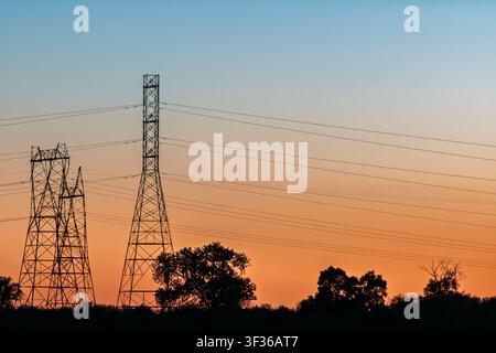 Hochspannungs-Freileitungsmasten, die sich vor einem farbenfrohen Sonnenuntergangshimmel abzeichnen. Stockfoto