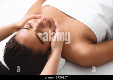Ziemlich schwarze Dame mit Lifting Gesicht Massage im Spa Stockfoto