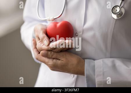 Gekürzte Nahaufnahme einer gealterten Ärztin, die ein Spielzeugherz in den Händen hält Stockfoto