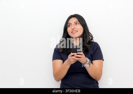 Fröhliche junge lateinamerikanische Frau zeigt auf ihr Smartphone in der Hand, Online-Shopping-Anwendung auf weißem Hintergrund Stockfoto