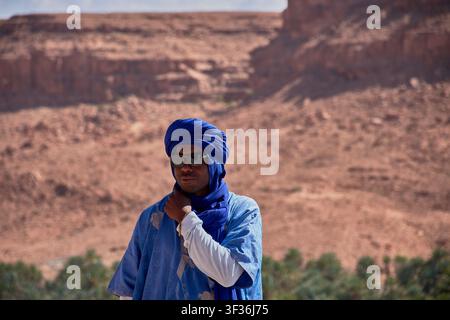 Tafilalet-Palmenhain, Marokko, 30. Mai 2026, Ein Mann in einem traditionellen blauen Berber-Tunika und Turban posiert in einer Mittelaufnahme vor der atemberaubenden n Stockfoto