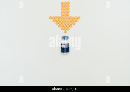 Gelbe Pillen bilden einen Pfeil, der auf eine Medicineflasche auf einem weißen Hintergrund zeigt. Stockfoto