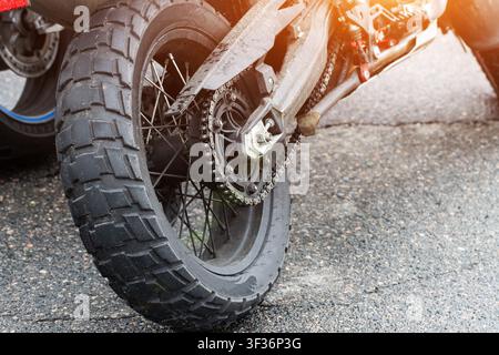Detailaufnahme des Hinterrads eines Motorrads, robuster Antriebskette und genopptem Reifen, der Schmutz und Staub von der Reise zeigt. Hinterradaufhängung und Speichen sind sichtbar Stockfoto