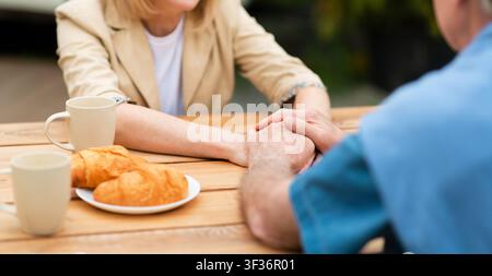 Nicht erkennbares Seniorenpaar, das beim Frühstück im Freien Hände hält, Nahaufnahme. Panorama Stockfoto