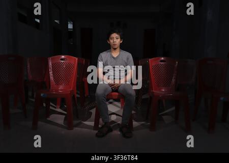 Einsamer Mann sitzt vor leeren Theatermöbeln und starrt in die Kamera in einer dunklen, stillen Halle mit einer gespenstischen Atmosphäre. Stockfoto