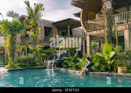 Frau entspannt sich an einem Wasserfall-Brunnen in der Bambus-Pool-Villa, Ninh Binh, Vietnam Stockfoto
